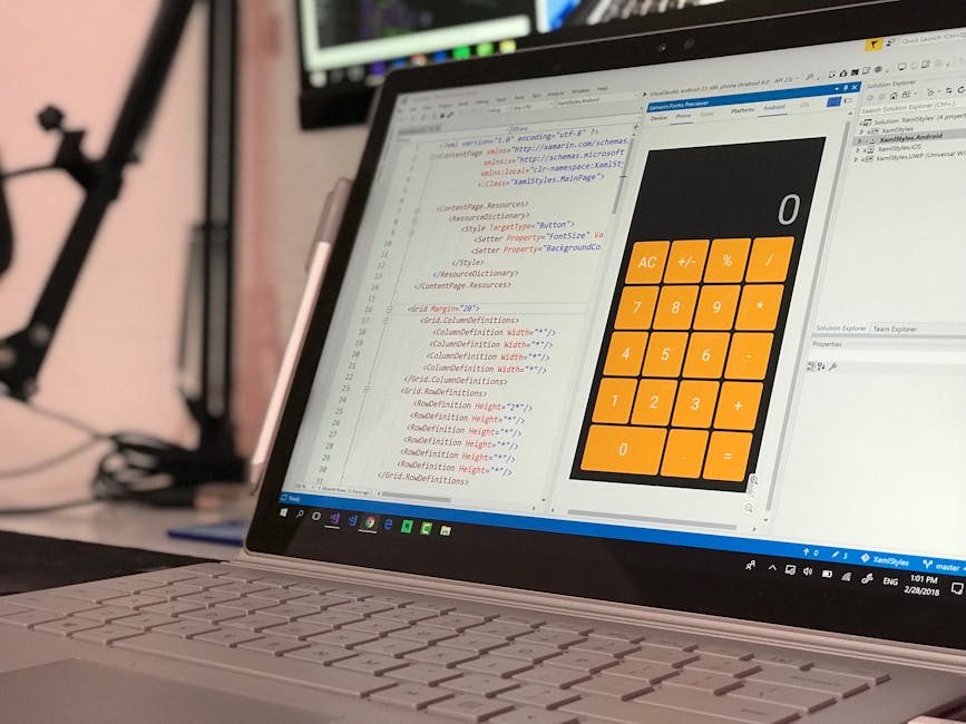 A close-up image of a laptop computer displaying lines of HTML code on the left side of the screen and a digital calculator interface with orange buttons on the right side. The laptop has a silver bod